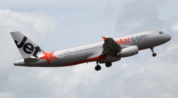 Side on photo of an aeroplane flying in the sky with Jetstar branding. 